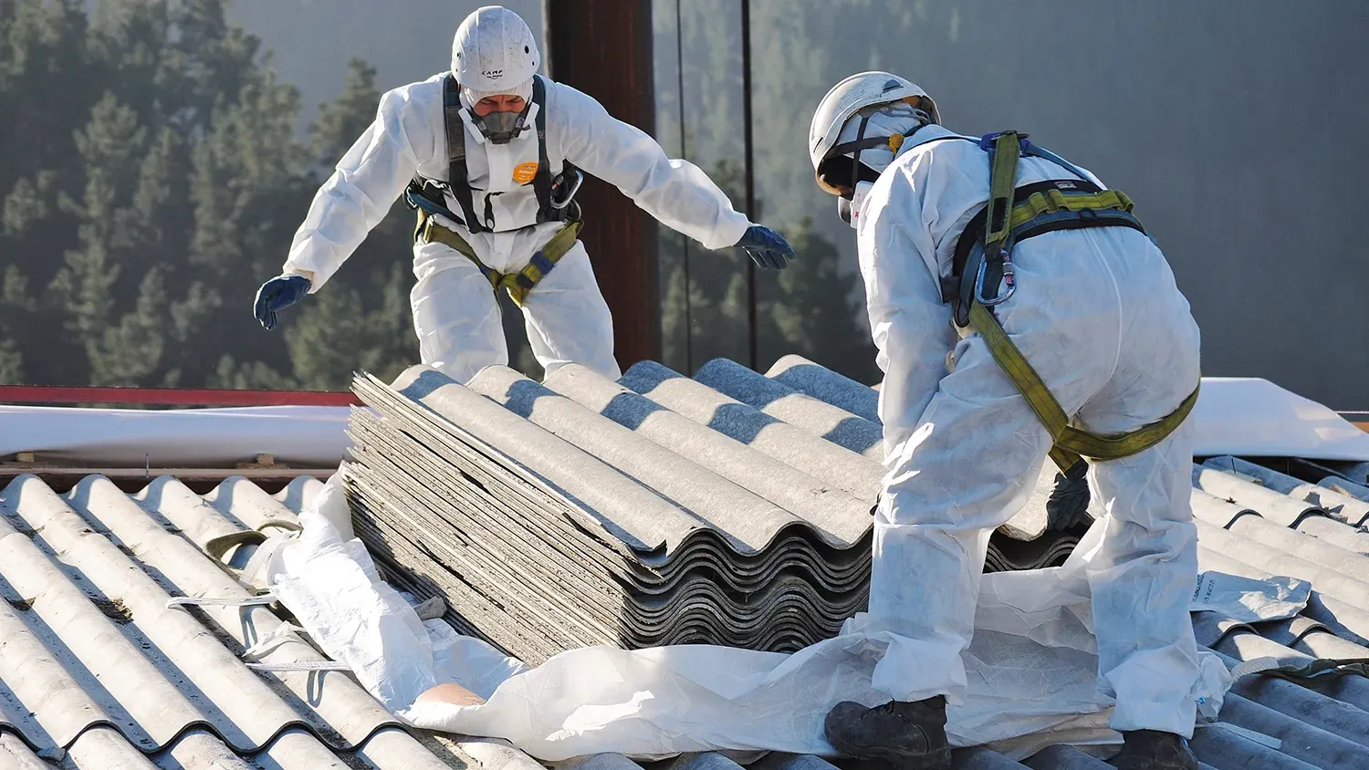 Workers in protective gear handling asbestos cement sheets on a roof.