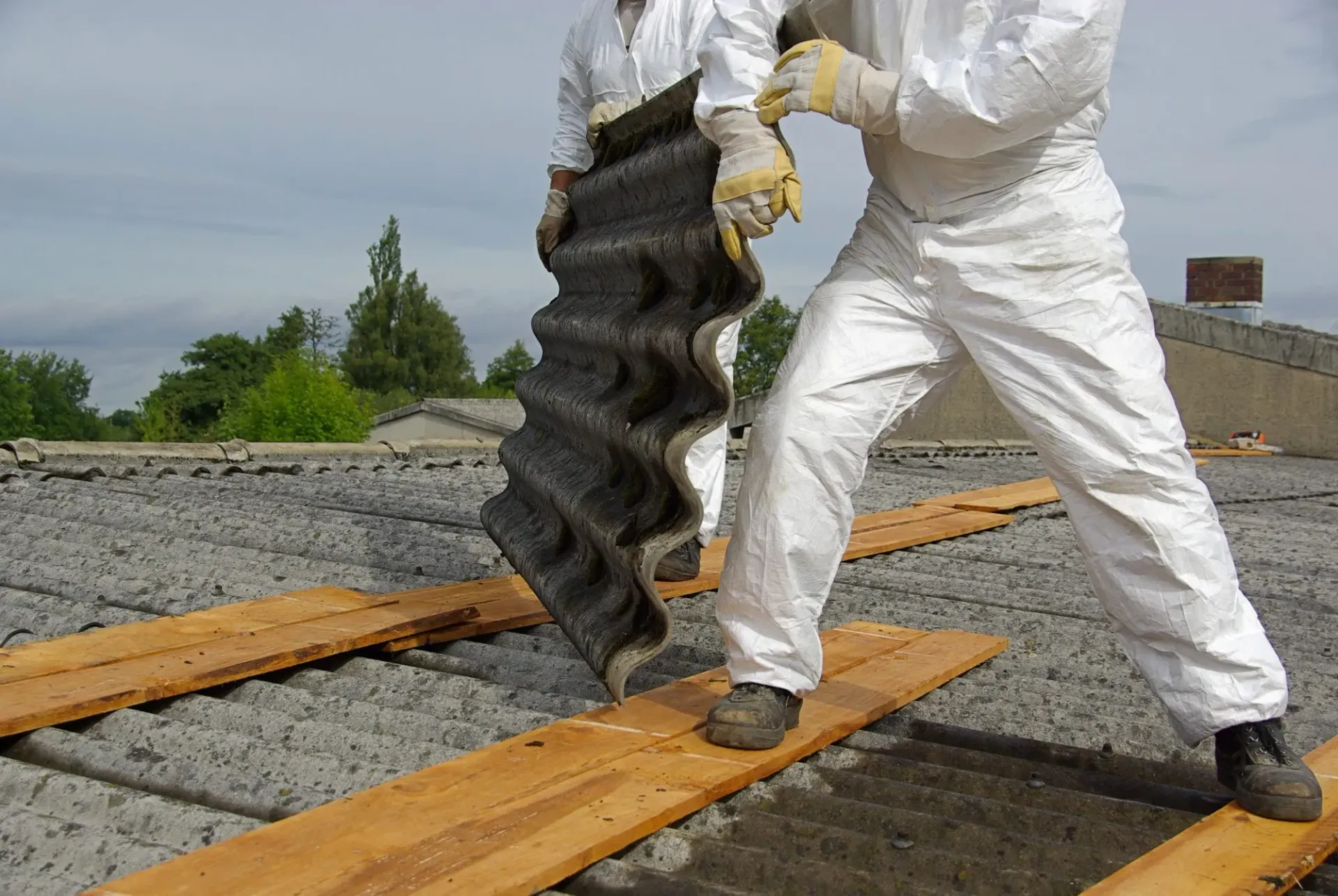 Asbestos removal workers in protective gear on a roof with asbestos cement sheets