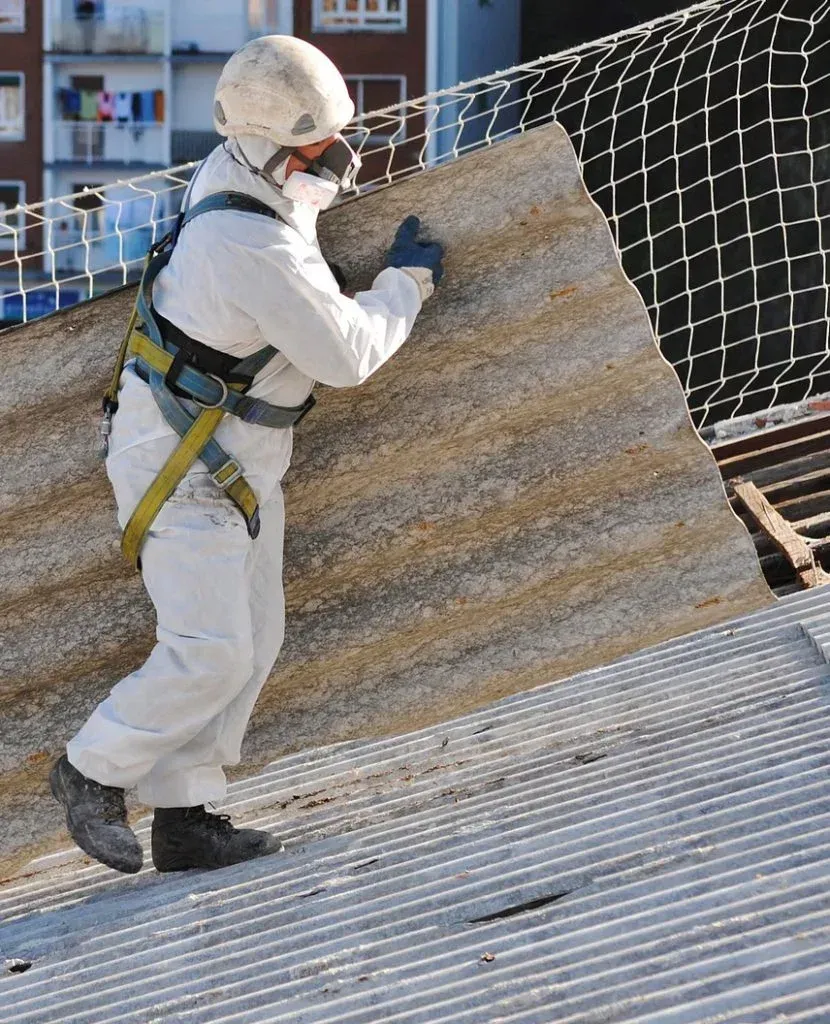 Asbestos removal worker in PPE handling corrugated roof sheet.