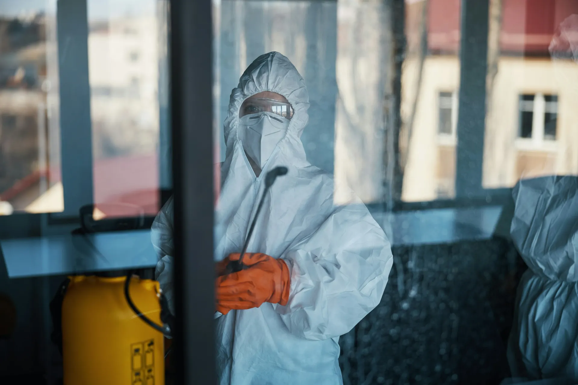 Worker in asbestos PPE spraying in a work area during clearance testing.
